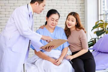 Obraz premium Asian man professional doctor visiting ward talking giving report good news to smiling and happy family and senior woman patient sitting on hospital bed with lovely daughter showing healthcare support