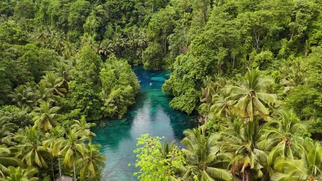 4k drone video panning around a small rowing boat floating in Paisupok Lake, one of the clearest lakes in the world, surrounded by jungle landscapes in the Banggai Islands, Sulawesi, Indonesia