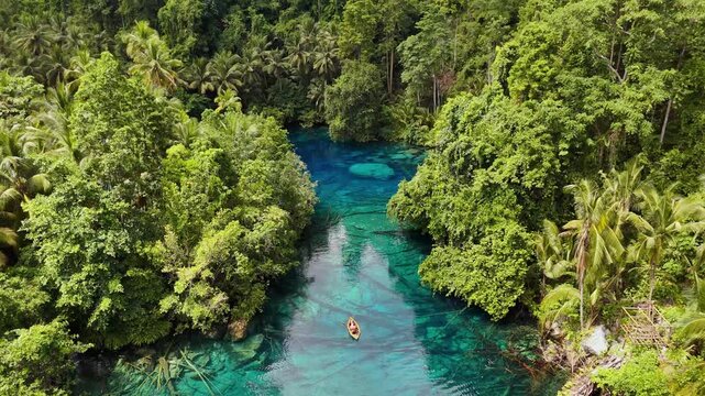 4k Drone video of a couple rowing in a small wooden boat through the clearest and beautiful blue water at Paisupok Lake in the Banggai Islands, Sulawesi