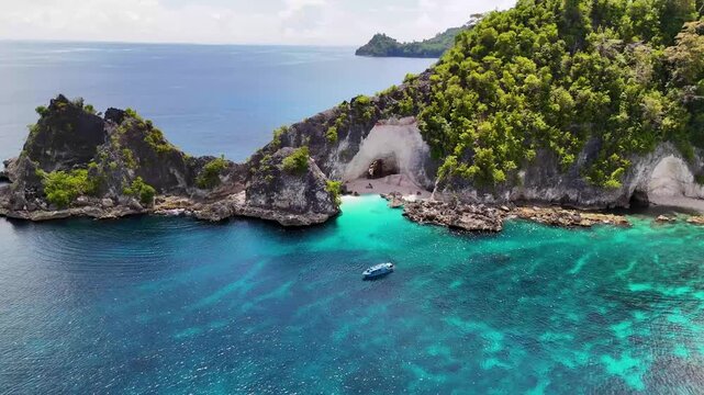 4k drone video of people sat on a white sand beach on a remote island with a cave in The Banggai Islands in Sulawesi, Indonesia. This is Batu Lobang Beach a popular beach for tourists to visit.