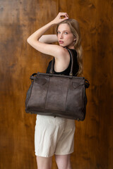 Fototapeta premium A beautiful fair-skinned model with wavy blonde hair in a half-body portrait, showcasing a minimalist black vest, wide-leg trousers, and a brown leather bag strap
