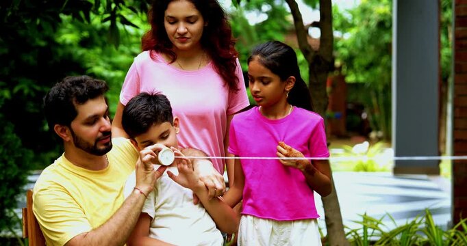 Indian family playing with string telephone in home garden, enjoying creative outdoor activity, spending quality fun time together with kids, parents, siblings, smiling and bonding joyfully