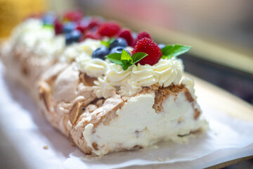 Meringue roll, dusted with powdered sugar, decorated with blueberries, raspberries and mint leaves on a white background with a blurred bokeh effect. Meringue roll. Festive baking. Pavlova dessert.