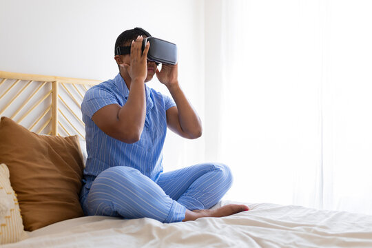 Woman wearing virtual reality headset sitting on bed at home