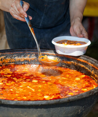 A person is serving soup from a large pot into a white bowl