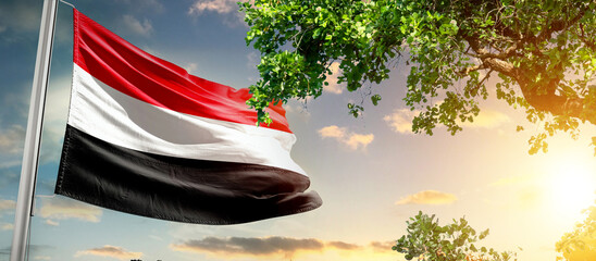 Yemen national flag waving in the sky behind the tree. The flag blow in beautiful sunlight. Yemen national flag for independence day.