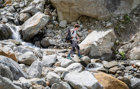 Man hiking across rocky alpine stream in summer mountains