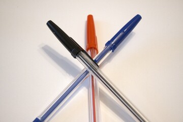 Three pens – red, black, and blue – arranged on a white background. Stationery concept with copy space. Close-up view.
