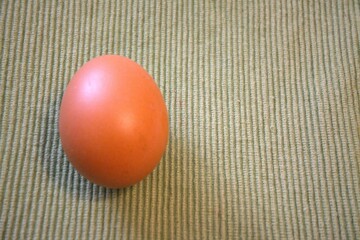 One brown chicken egg placed on green textile fabric, shown in a close-up with room for text. Natural, minimal style.