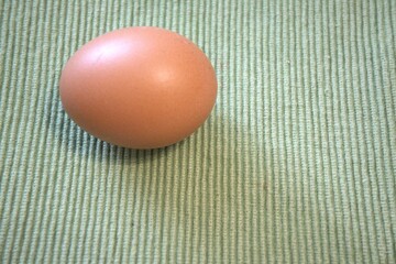 One brown chicken egg placed on green textile fabric, shown in a close-up with room for text. Natural, minimal style.