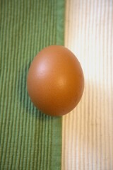 Single brown egg on a background of green and white fabric. Close-up with minimalist composition and copy space.
