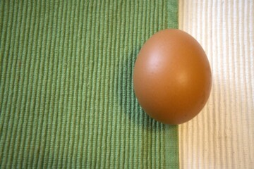 Single brown egg on a background of green and white fabric. Close-up with minimalist composition and copy space.
