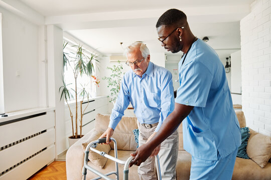 Doctor or nurse caregiver with senior man using walker assistanece at home or nursing home