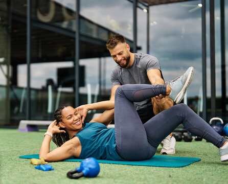 Portrait of  healthy fit woman duing crunches at the gym supprted by a trainer instructor exercising in fitness club