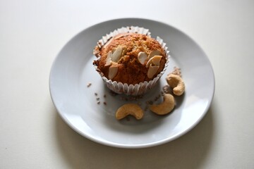 Close-up of a gluten-free and sugar-free almond muffin served on a white plate with cashew nuts and sesame seeds. A healthy, diet-friendly dessert perfect for clean eating.