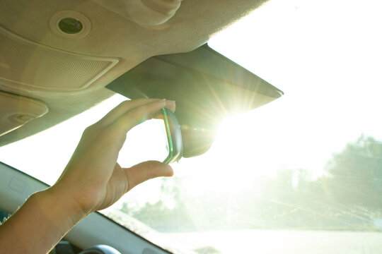 Female hand adjusting rearview mirror in car against sunlight through windshield