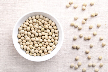 Dried green peas in white bowl on linen. Seeds of Pisum sativum, a pulse, vegetable and fodder crop, that can be reconstituted in hot water. Good source of protein, fiber, magnesium, and potassium.