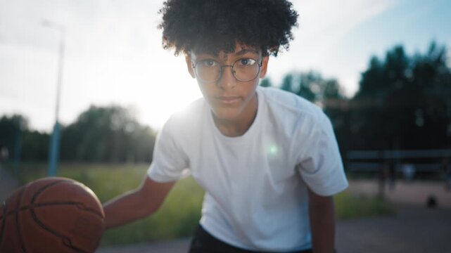 African american teen boy practicing basketball exercises with ball, portrait. Sport and active hobby for young people and children, teenager training alone on outdoor court, looking at camera