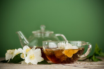 Aromatic tea with jasmine flowers in a glass cup on a green background