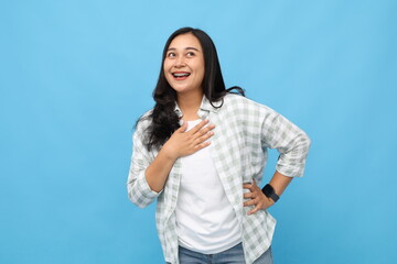 Young cheerful asian woman putting hand on chest, in good mood, laughing happily wearing casual clothes, isolated over blue background.