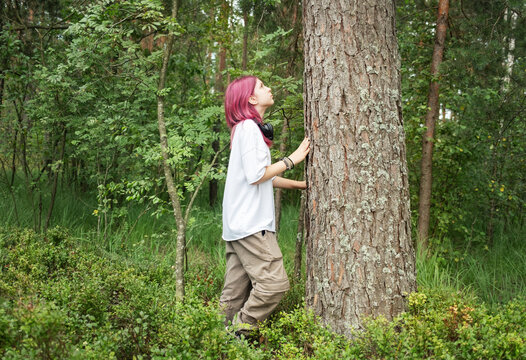 Young woman with pink hair embracing a tree in a forest, enjoying nature