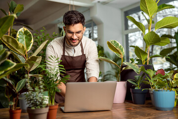 Male shop assistant in the flower shop working on a laptop