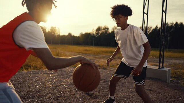 Young black streetballer bouncing ball and attacking basket, slow motion shot. Basketball match on outdoor court in summer day, active lifestyle and sport, teenagers practicing, future champions - Powered by Adobe