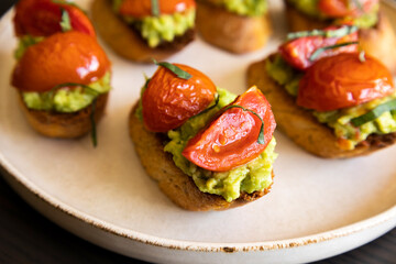avocado crostini topped with roasted cherry tomatoes and fresh basil, served as a bite-sized party appetizer. Perfect for food blogs, entertaining ideas