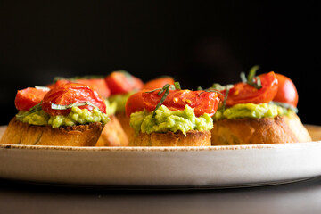 avocado crostini topped with roasted cherry tomatoes and fresh basil, served as a bite-sized party appetizer. Perfect for food blogs, entertaining ideas