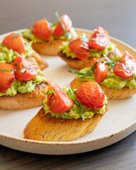 avocado crostini topped with roasted cherry tomatoes and fresh basil, served as a bite-sized party appetizer. Perfect for food blogs, entertaining ideas