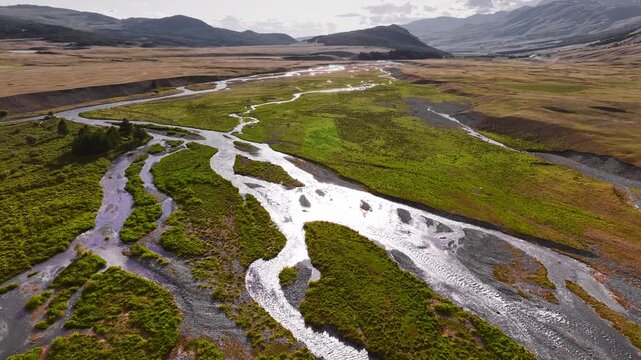 Meandering stream and river against the backdrop of mountains and clouds on the Ukok plateau, Altai Republic. Drone and aerial view. Nature, natural places. Village life.