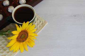 a box of chocolates with a cup of coffee and a small sunflower early in the morning
