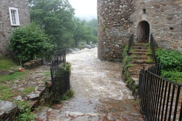 Flooded pathway between stone buildings and a medieval-style stone tower