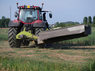 Fototapeta premium Farmer Operating Red Tractor With Mower Attachment Working In Field