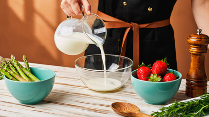 Culinary Creation Pouring Creamy Base for Dessert, Close-up, overhead shot of a hand pouring a creamy white liquid from a clear glass pitcher into a large glass bowl, preparing a dessert or sauce.