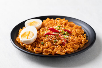 Spicy Korean dried instant noodles with boiled egg, sliced scallions, sesame seed and fresh chili on white background