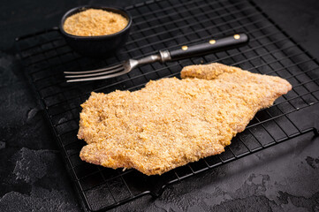 Raw breaded pork Schnitzel steak on a rack. black background. top view