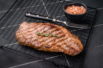 Grilled Striploin steak, New York strip beef meat steak on a rack. black background. top view