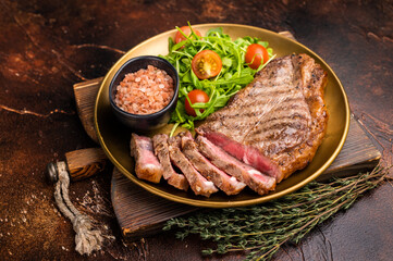 Grilled New York strip steak, beef meat steak on a plate with salad. brown background. top view
