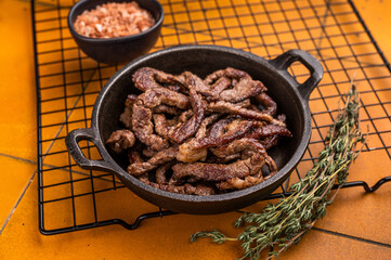 Fried beef tender strips, sliced steak in a skillet. orange background. top view
