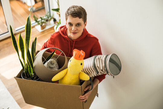 Woman happily moving belongings at home holding a box with household items