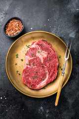 Raw Rib eye steak with herbs and spice in plate, fresh beef meat. black background. top view