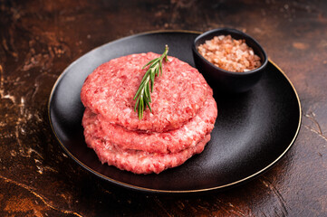 Raw veal and beef minced meat cutlets for burgers with herbs on plate. brown background. top view