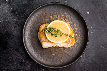 Roast Halibut fish loin fiilet on plate. Black background. top view
