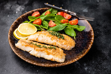 Roast Cod fish fiilets, white fish meat on plate with salad. Black background. top view