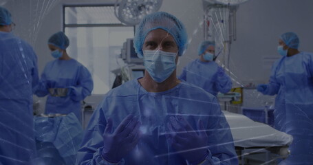 Facing camera Asian surgeon in blue scrubs adjusting gloves in operating room, with overhead lights