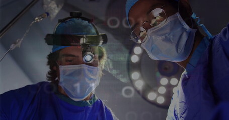 Two surgeons in blue scrubs operating in operating room, with overhead light and digital overlays
