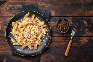 Italian Carbonara pasta topped with crispy bacon bits in a plate. Wooden background. Top view