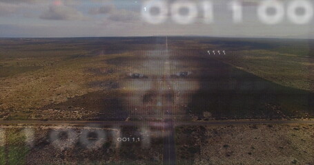 Hovering holographic male face streaming binary code across arid scrubland plain, with dirt road