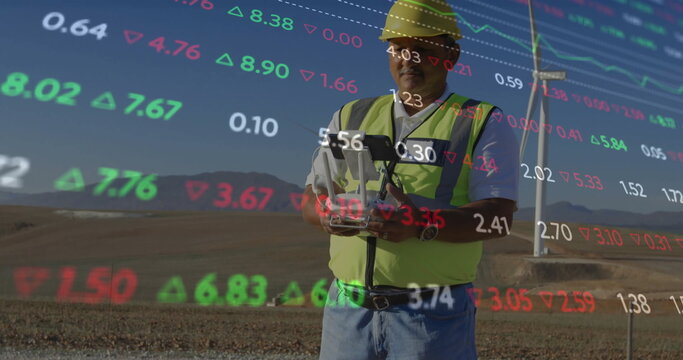 Operator in yellow helmet, neon vest operating tablet at wind turbine, overlaid data, copy space